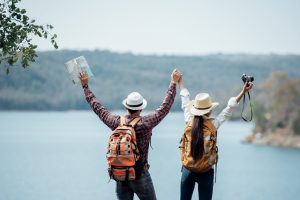 A mand and a women travelling together standing in front of a lake with their hands raised high