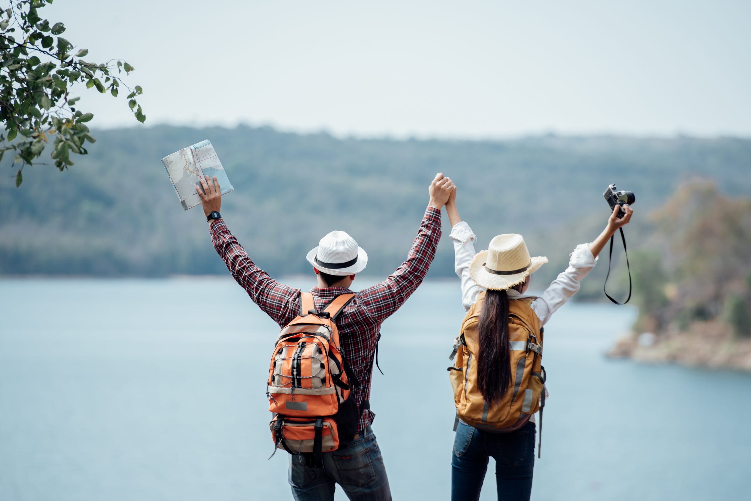 A mand and a women travelling together standing in front of a lake with their hands raised high