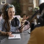 A women part of a podcast sitting in front of a mic smiling