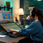 A animation artist women working on a laptop sipping coffee with headphones on