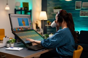 A animation artist women working on a laptop sipping coffee with headphones on
